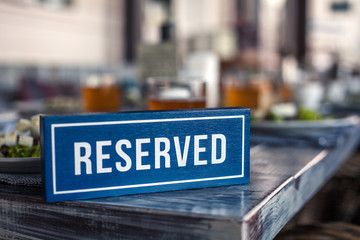 A wooden blue and white rectangular plate with the inscription Reserved stands on the corner of a gray aged vintage table. Concept of lunch in a restaurant, holiday, banquet