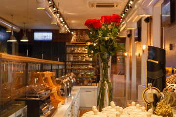 A bouquet of red roses in a transparent high vase stands on the bar counter of the restaurant. Concept cozy interior, view of hall, delicious lunch, beautiful flowers