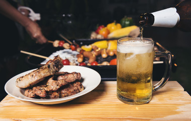 pouring beer with barbecue pork grill in background.