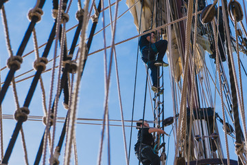 Sailors work with sails at a height on a traditional sailboat
