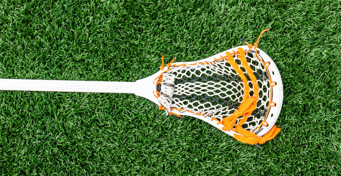 Lacrosse stick on green turf with orange stiching