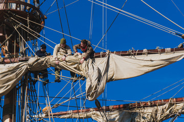 Sailors work with sails at a height on a traditional sailboat