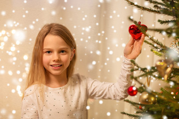 christmas, holidays and childhood concept - happy girl in red dress decorating natural fir tree