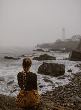 woman walking along a foggy coast with lighthouse