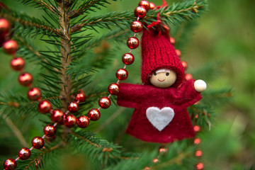 Christmas tree toy in the form of a little girl in a red dress and a hat with a white heart of felt on her chest. New Year's theme, style red and green.