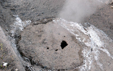 Steam is from sanitary sewer cover in snow on the roadside. Top view. Close-up.