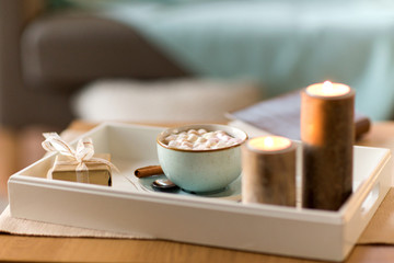 Fototapeta na wymiar holidays and still life concept - hot chocolate with marshmallow, christmas gift and candles on table
