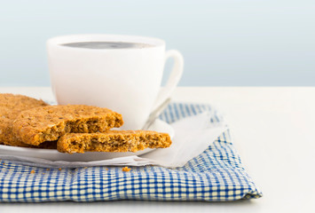 Homemade shortbread cookies made of oatmeal are stacked with hot coffee cup on cloth and paper on white table background. Concept food healthy snack for enjoy in holiday.