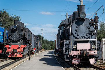 Old steam locomotive beside a railway station platform. Retro train.