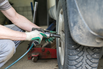 car mechanic screwing or unscrewing car wheel of lifted automobile at repair service station