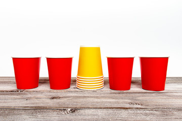 Four red and stack of yellow paper disposable cups for coffee and nonalcoholic drinks on wooden background