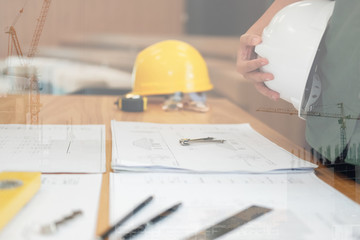 engineer architect worker holding safety helmet hardhat wtih construction blueprint on desk