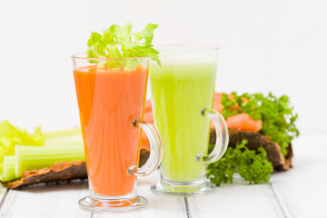 Carrot and celery juice with fresh vegetables on bark plates on wooden background.