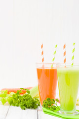 Carrot and celery juice with fresh vegetables on bark plates on wooden background.