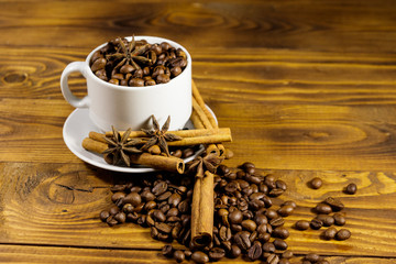 Coffee beans in white cup, cinnamon sticks and star anise on wooden table