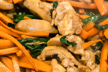 pieces of chicken meat frying with sliced carrots