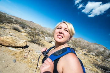 Female blonde hiker spots to squit to look off into the distance as she hikes through the California desert in the Coachella Valley