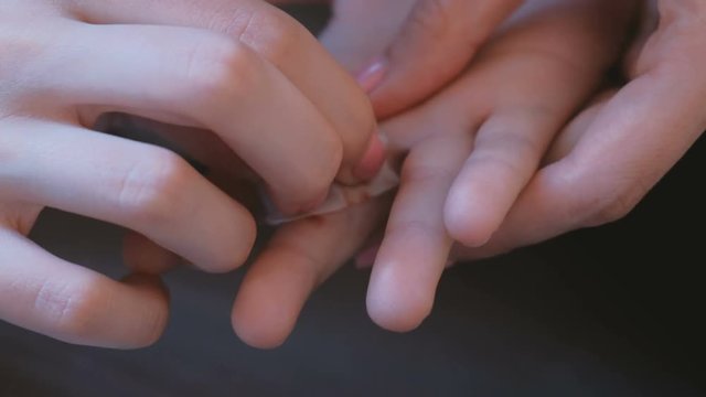 Mom processes the cut on the finger of her child with an alcohol napkin. Hands close-up.