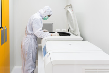 A scientist in sterile coverall gown using laboratory equipment for doing biological research in...