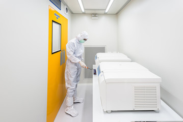 A scientist in sterile coverall gown using lint roller for cleaning laboratory. Cleanroom facility.