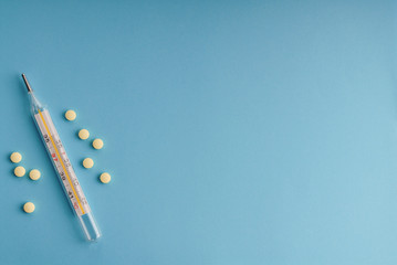 Pills and a traditional thermometer on blue.