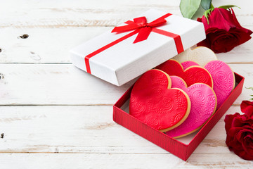 Heart-shaped cookies in gift box decorated with roses for Valentine's Day on white wooden table....