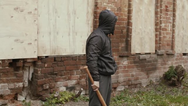 Aggressive bandit in black mask and hood ganging with baseball bat outdoors