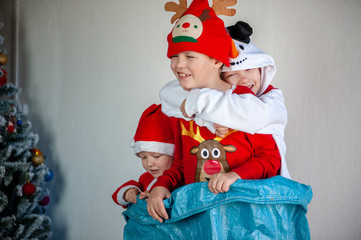 Cute boys dressed in festive costumes of Santa Claus and snowmen and decorate Christmas tree with balls and garlands. Children play and wait for gifts. Christmas Eve