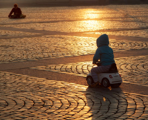 A child on a scooter riding on the cobbled square of the old city in the rays of the sunset evening...
