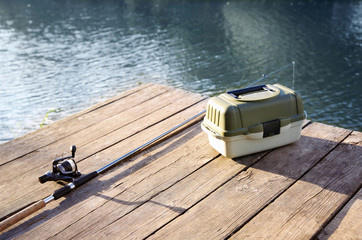 Tackle box and rod for fishing on wooden pier at riverside. Recreational activity