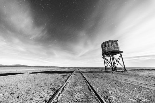 Old and abandoned railway track and station with it water tank to fill the trains during their travel around the Atacama Desert for transporting niter coming from the mining industry, full moon scene