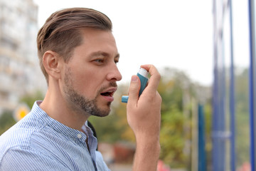 Man using asthma inhaler outdoors. Health care - obrazy, fototapety, plakaty