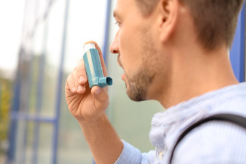 Man using asthma inhaler outdoors, closeup. Health care