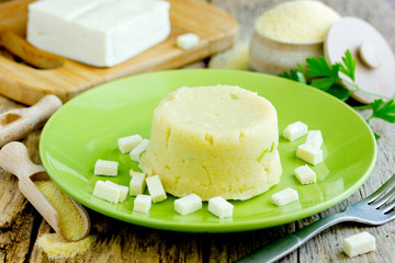 Polenta porridge with salty cheese on wooden table with ingredients