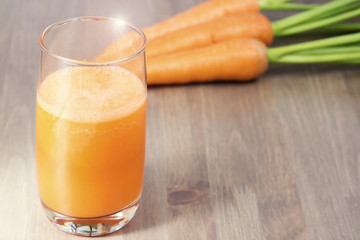 A glass of healthy carrot smoothie with carrots on wooden background