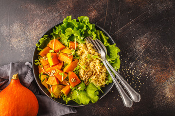 Warm quinoa and pumpkin salad in a white plate on dark background, top view.