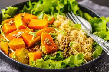Warm quinoa and pumpkin salad in a white plate on dark background.