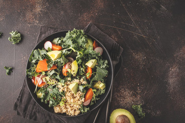 Avocado, quinoa, yam and kale salad in black plate on a dark background.