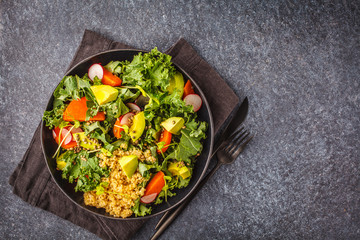 Avocado, quinoa, yam and kale salad in black plate on a dark background.