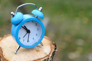 A blue alarm clock stands on the surface of a felled tree stump . The concept of time.