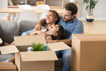 Multi-ethnic family spend time together sitting on couch in living room have fun play with little preschool daughter surrounded by cardboard on boxes at home. Buying new house moving mortgage concept