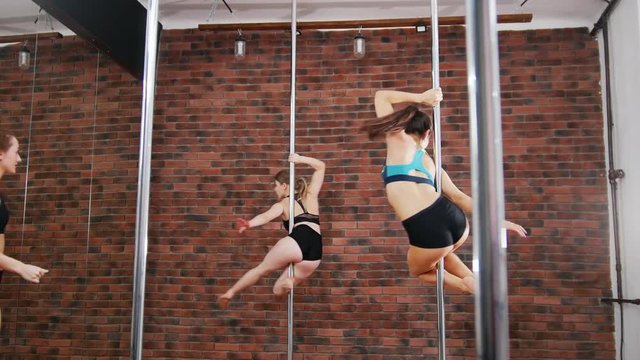 Two women practicing a pose in a pole fitness class. Dynamic pylon