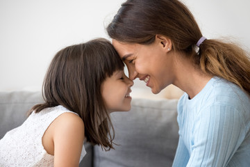 Close up profile faces smiling mother and daughter touching with foreheads with closing eyes. Mom...