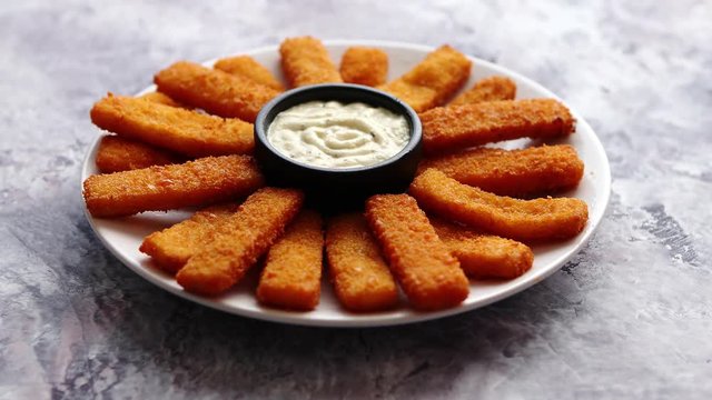 Crumbed fish sticks served with garlic dip sauce on a white plate on a stone table. Top view with copy space.