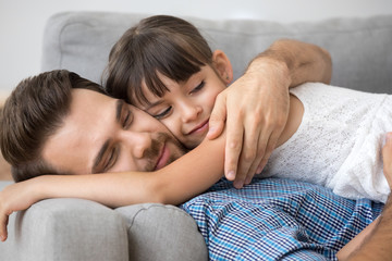 Obraz na płótnie Canvas Diverse multi-ethnic family indoors. Close up small daughter hugging loving father lying together on couch at home. Love tenderness understanding and warm relationship between parent and kid concept