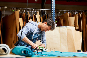 Male Worker Cutting Fabric With Rotary Cutter In Sofa Workshop