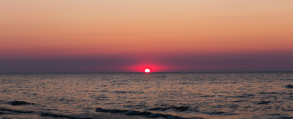 Red sun on a sunset. Sunset on the sea. Beautiful evening landscape. Waves in a sea on a sunset. Panorama