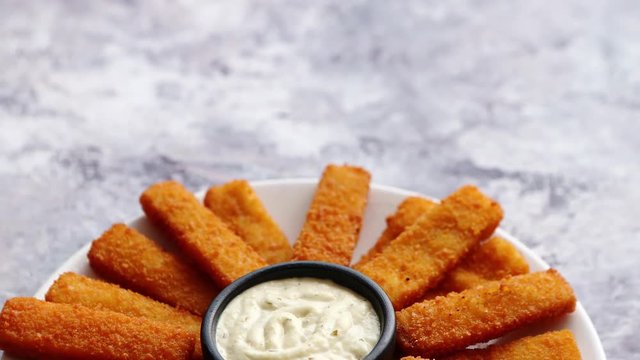 Crumbed fish sticks served with garlic dip sauce on a white plate on a stone table. Top view with copy space.