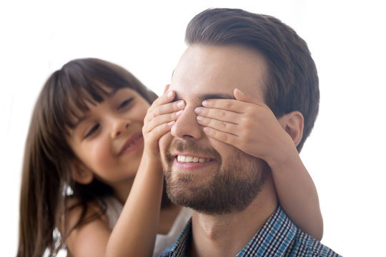 Close up portrait young male with closed eyes indoors. Happy cheerful little daughter playing covering daddy eyes with hands prepare for him surprise make a gift at fathers day. Life events concept