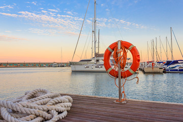 the quay of a marina at  the sunset /a mooring rope with a lifebelt  on  the quay of a marina at  the sunset - obrazy, fototapety, plakaty